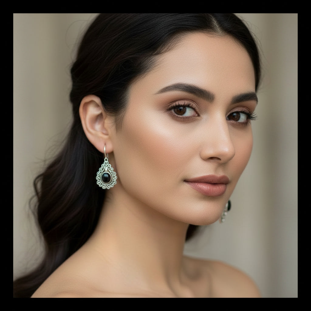 A pair of ornate silver-toned teardrop earrings with black oval center stones, worn beautifully as a statement.
