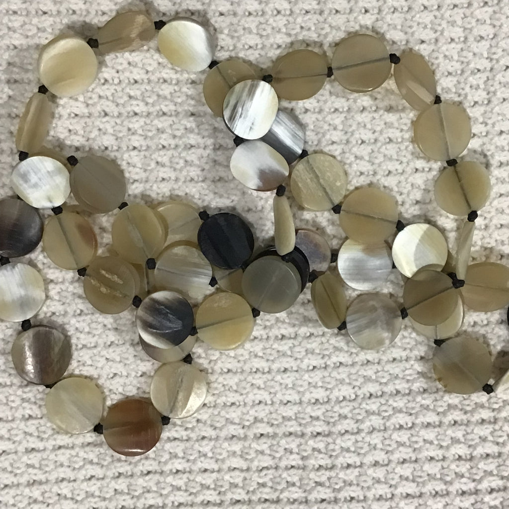 A strand of round shell beads, made from buffalo horn in natural beige, cream, and brown tones with some darker marbled pieces, strung on a black cord, individually knotted.